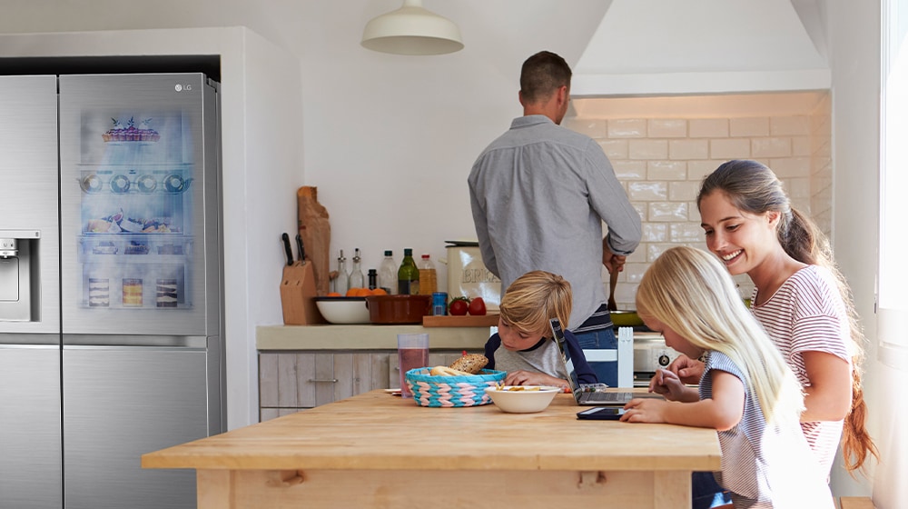 The whole family is sitting at the table preparing a meal. InstaView refrigerator installed on one side of the kitchen is creating cool air quickly.