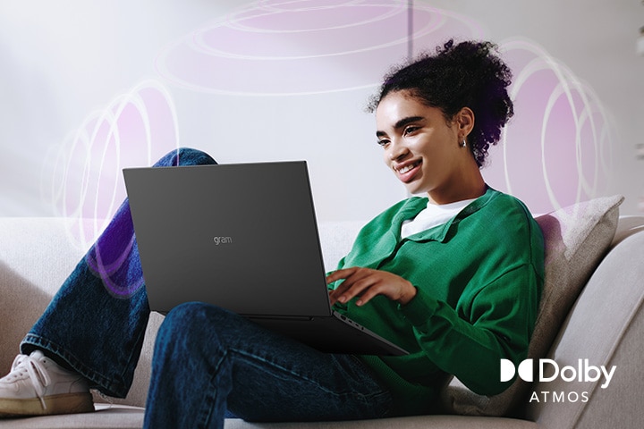 A person sitting on a couch, enjoying immersive audio while using an LG gram laptop. The text highlights Dolby Atmos technology, emphasizing a rich, expansive, 360-degree auditory experience. Surrounding sound waves in the background visually represent the immersive soundscape.