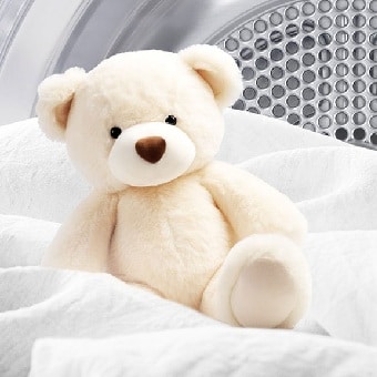 Image of a blanket and teddy bear inside a LG dryer with the British Allergy Foundation logo displayed