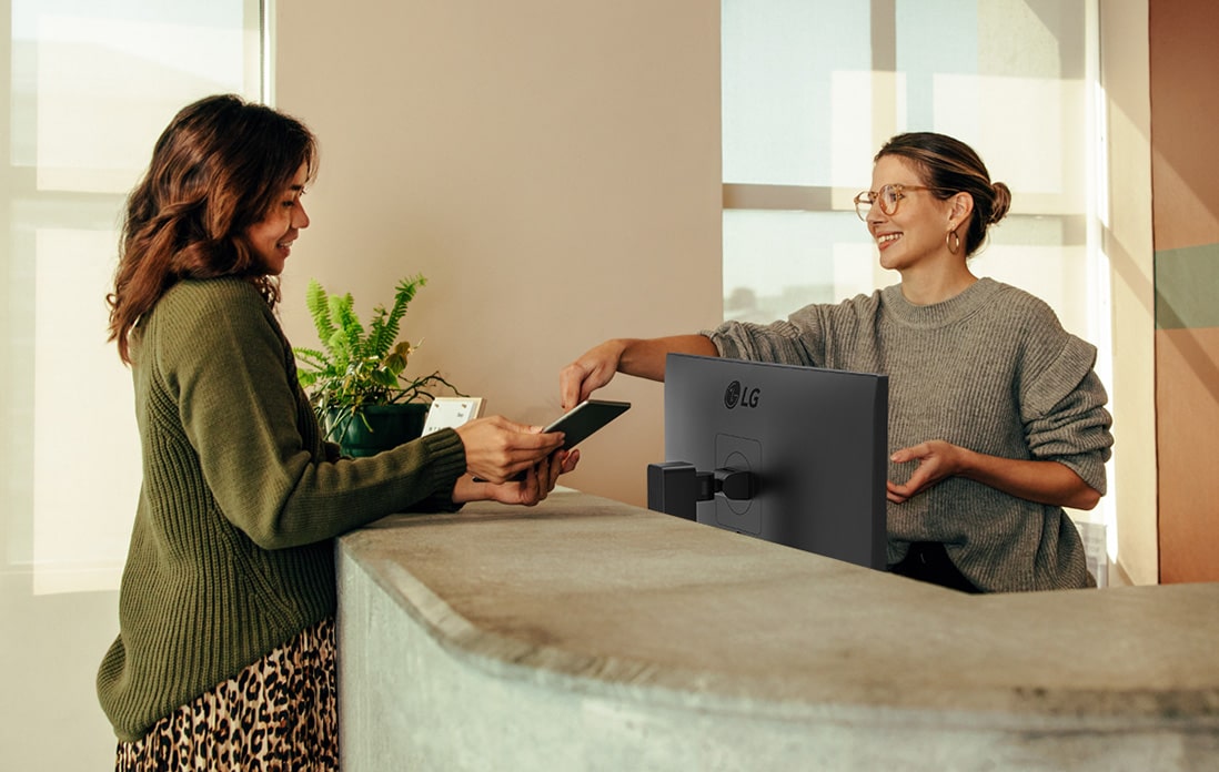 Friendly receptionist showing a woman where to sign on a digital tablet.	