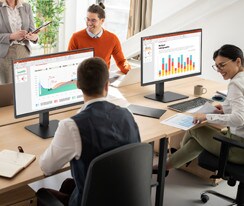 Employees sitting at office desks and having a conversation.	