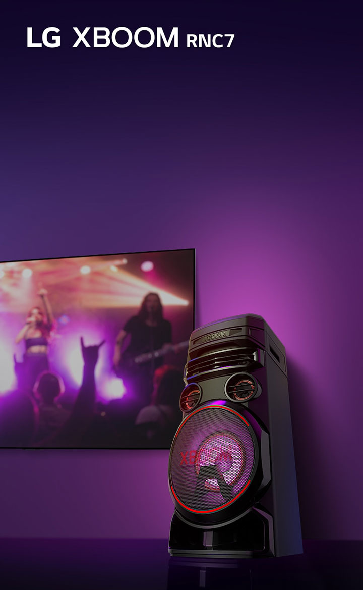 A low angle view of the right side of LG XBOOM RNC7 against a purple background. The XBOOM light are also purple. And a TV screen displays a concert scene.
