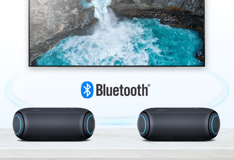 On a table, two LG XBOOM Go with sky blue lighting are in front of a TV showing a waterfall.