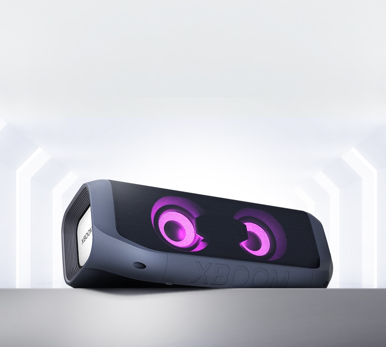 An LG XBOOM Go with magenta lighting is placed at an angle on a gray shelf.