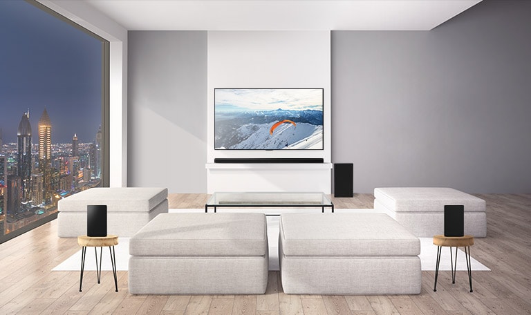 LG Soundbar with a sub-woofer and 2 rear upfiring speakers is in a living room. Graphics of soundwaves coming out from rear speakers to the ceiling and bounce back. (play the video)