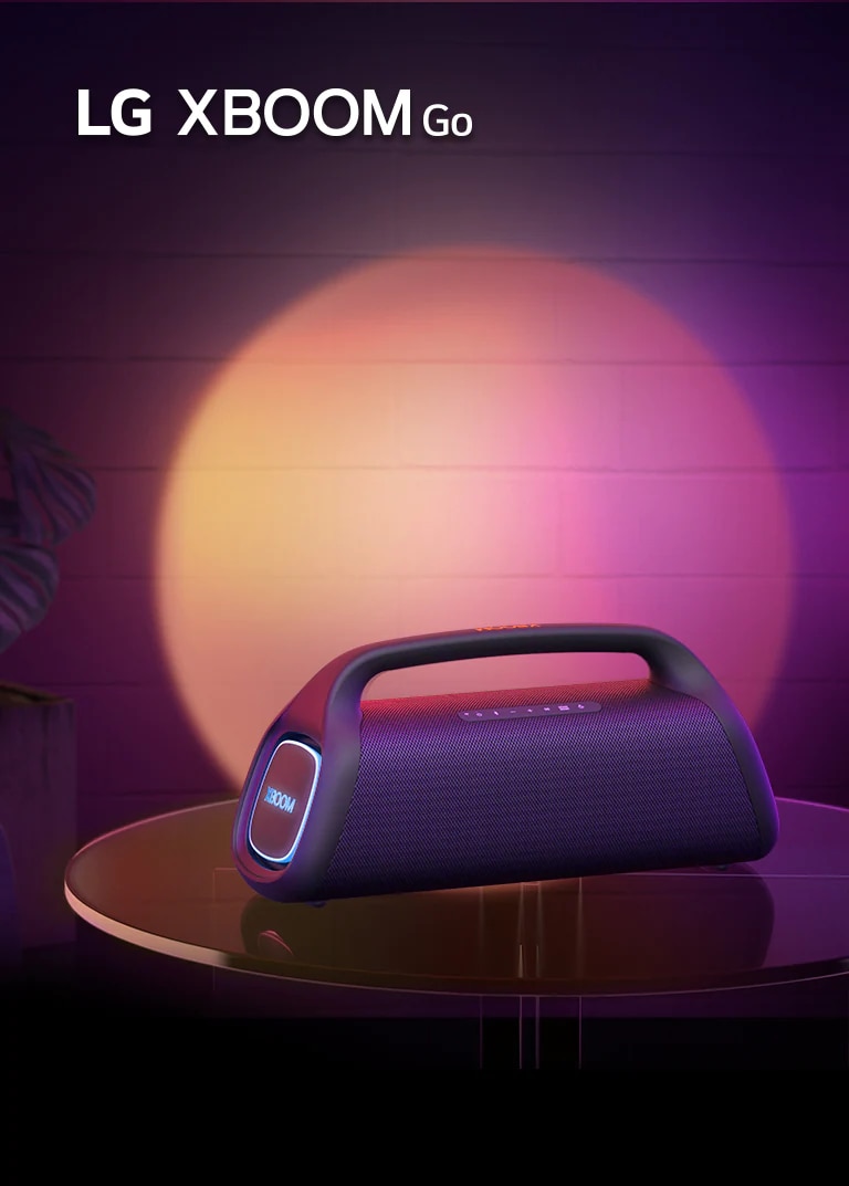 LG XBOOM Go XG9 is placed on the metal table with orange lighting is on. Behind the table, stage lighting is spotlighting the wall.