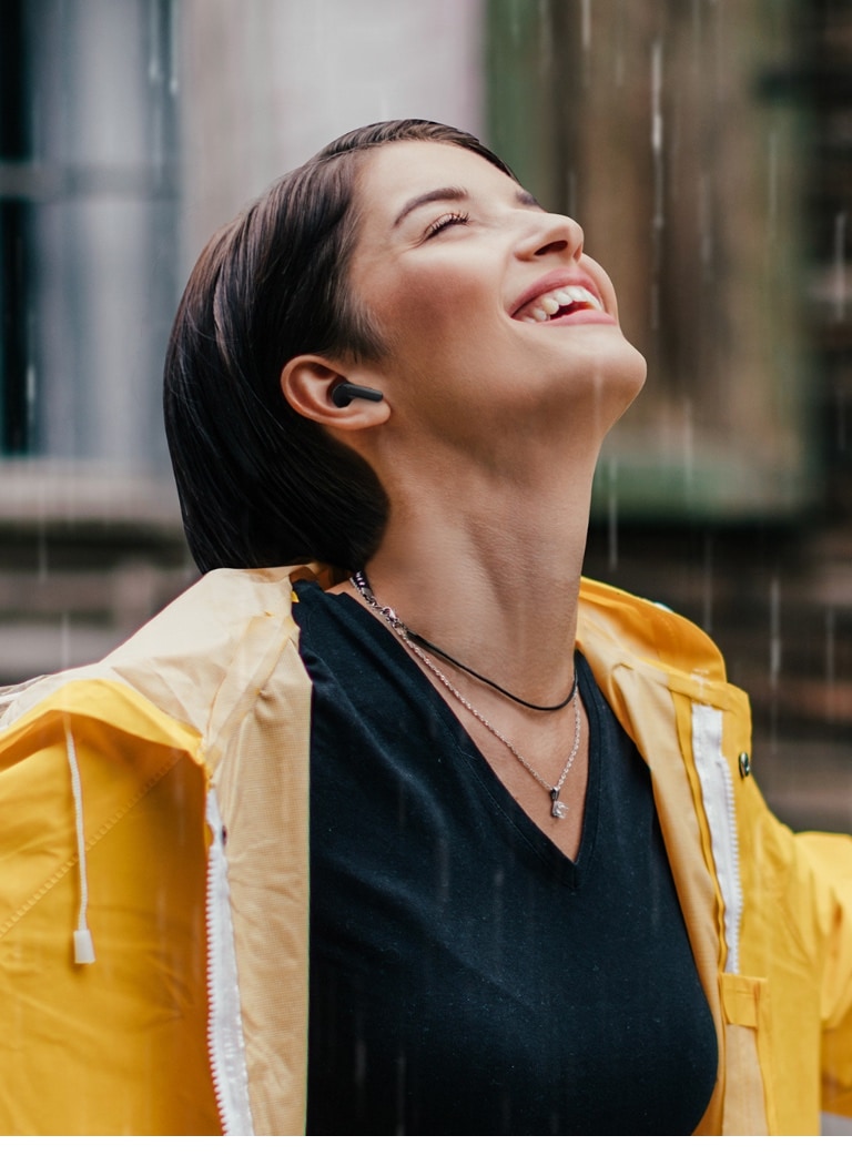 A woman wearing a bright raincoat listens to the earbuds while standing in the rain.