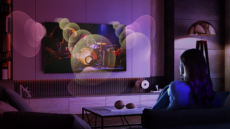A woman sits on a couch watching a concert with bubbles depicting surround sound around her.