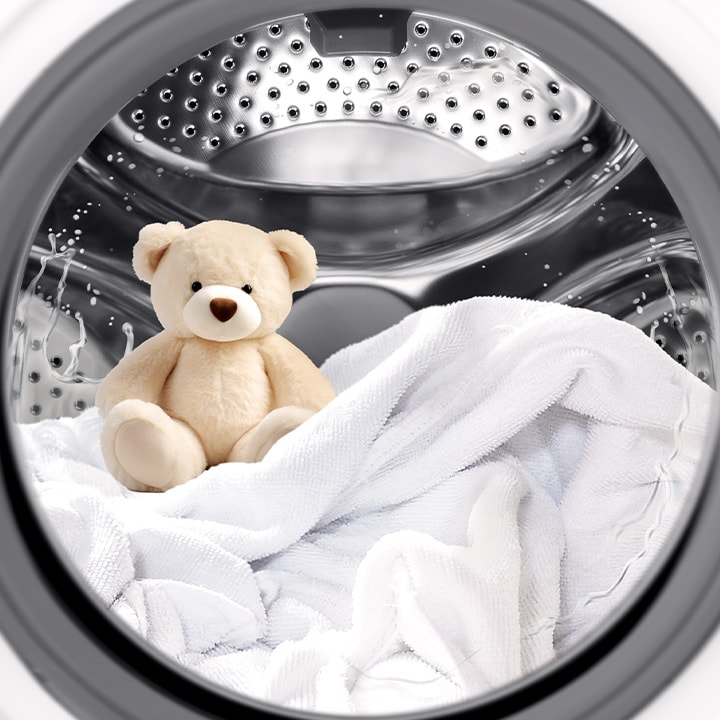 A stuffed animal and blanket inside a washing machine drum with laundry in progress