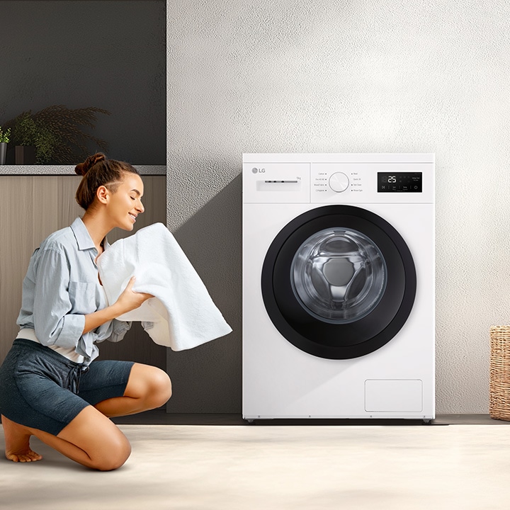 A woman kneeling in front of a washing machine in the living room, holding a clean blanket