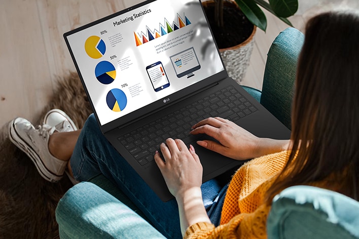 A person sitting comfortably in a chair, using a laptop that displays a presentation with charts and graphs. An animation demonstrates the anti-glare screen by showing no light reflection even when sunlight shines directly onto the display.	