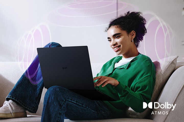 A person sitting on a couch, enjoying immersive audio while using an LG gram laptop. The text highlights Dolby Atmos technology, emphasising a rich, expansive, 360-degree auditory experience. Surrounding sound waves in the background visually represent the immersive soundscape.