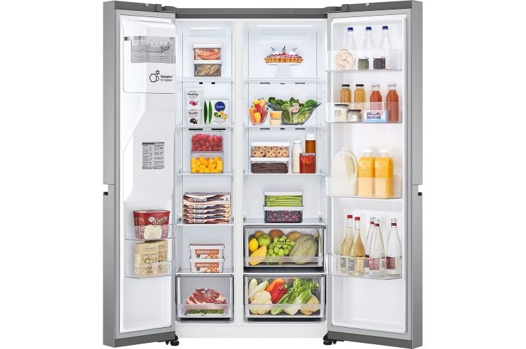 A fully stocked, open stainless steel side-by-side refrigerator filled with fresh fruits, vegetables, drinks, dairy products, and frozen goods. The right door contains beverages, and the interior lighting illuminates the well-organised shelves and bins.
