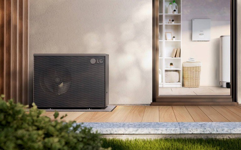 An LG outdoor heat pump unit installed on a wooden deck beside a modern home, with a view of an interior laundry room through a sliding glass door