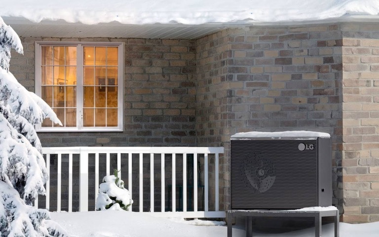 An LG heat pump system operating in a snowy environment outside a brick house, highlighting the unit's efficiency and reliability in winter conditions.