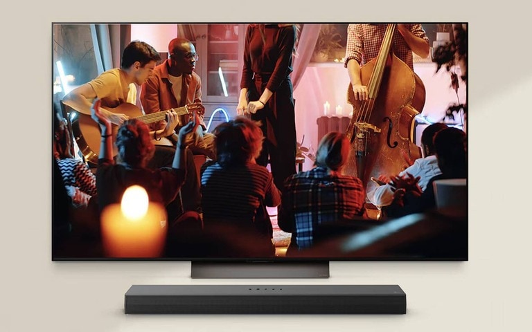 LG TV featuring a cozy live music performance with musicians playing guitar and double bass in a warmly lit setting. Below the LG TV, an LG soundbar is positioned, enhancing the immersive atmosphere.