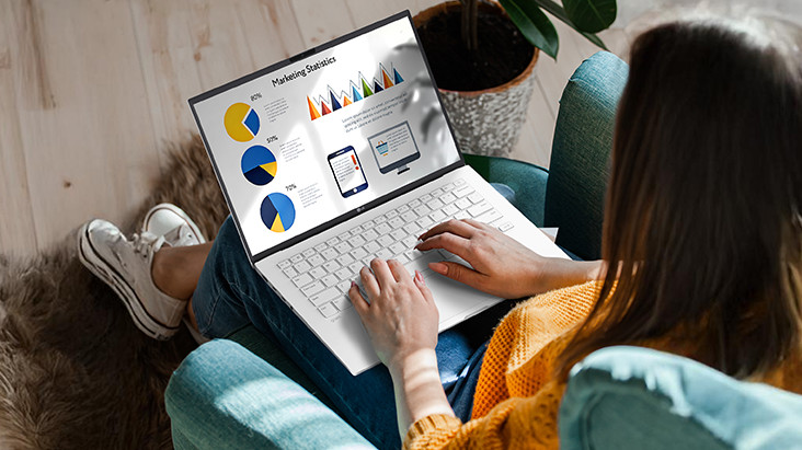 A person sitting comfortably in a chair, using a laptop that displays a presentation with charts and graphs. An animation demonstrates the anti-glare screen by showing no light reflection even when sunlight shines directly onto the display.