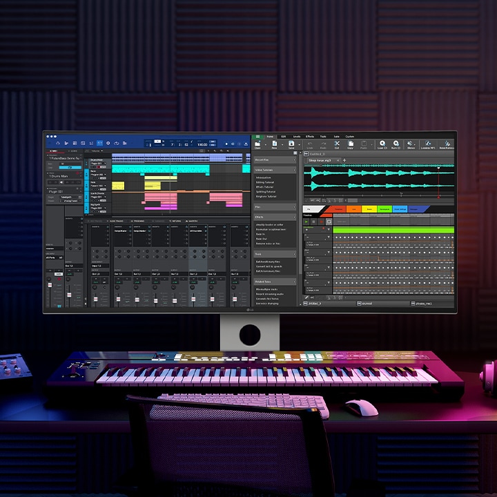 In a dark room with blue and violet lighting a UltraFine monitor stands with recording program on it. On the desk where it stands a keyboard, tablet, headphone and other accessories are placed.