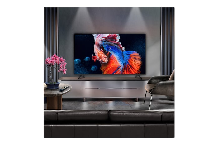 A family sits on a couch facing a LG QNED TV sitting above a TV stand with a little girl pointing to a screen depicting two dolphins. The title talks about how you can enjoy high resolution on a massive screen.