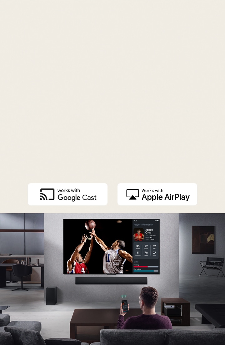Person in their living room holding their phone. On the phone is a transmitting icon showing that the phone screen is being mirrored on the TV. On the TV is a basketball game to the side is the mirrored screen, showing player statistics.