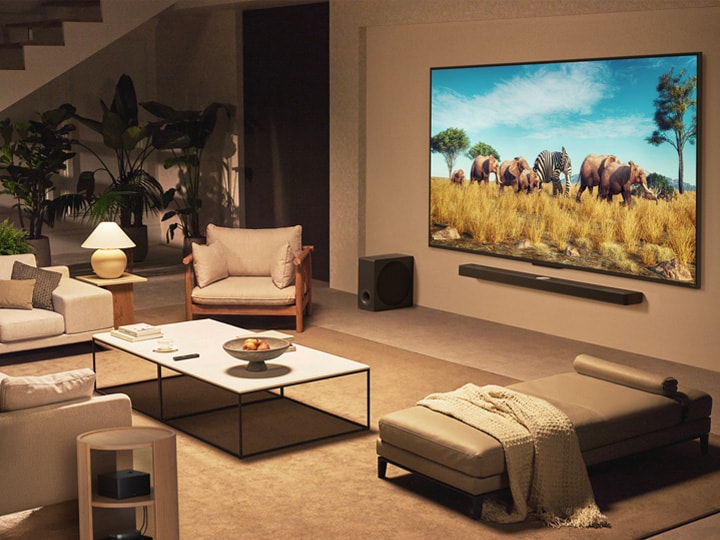 A family sits on a couch facing a LG QNED TV mounted on a wall above a LG Soundbar in a modern living room space. Zero Connect Box sits inside a coffee table.