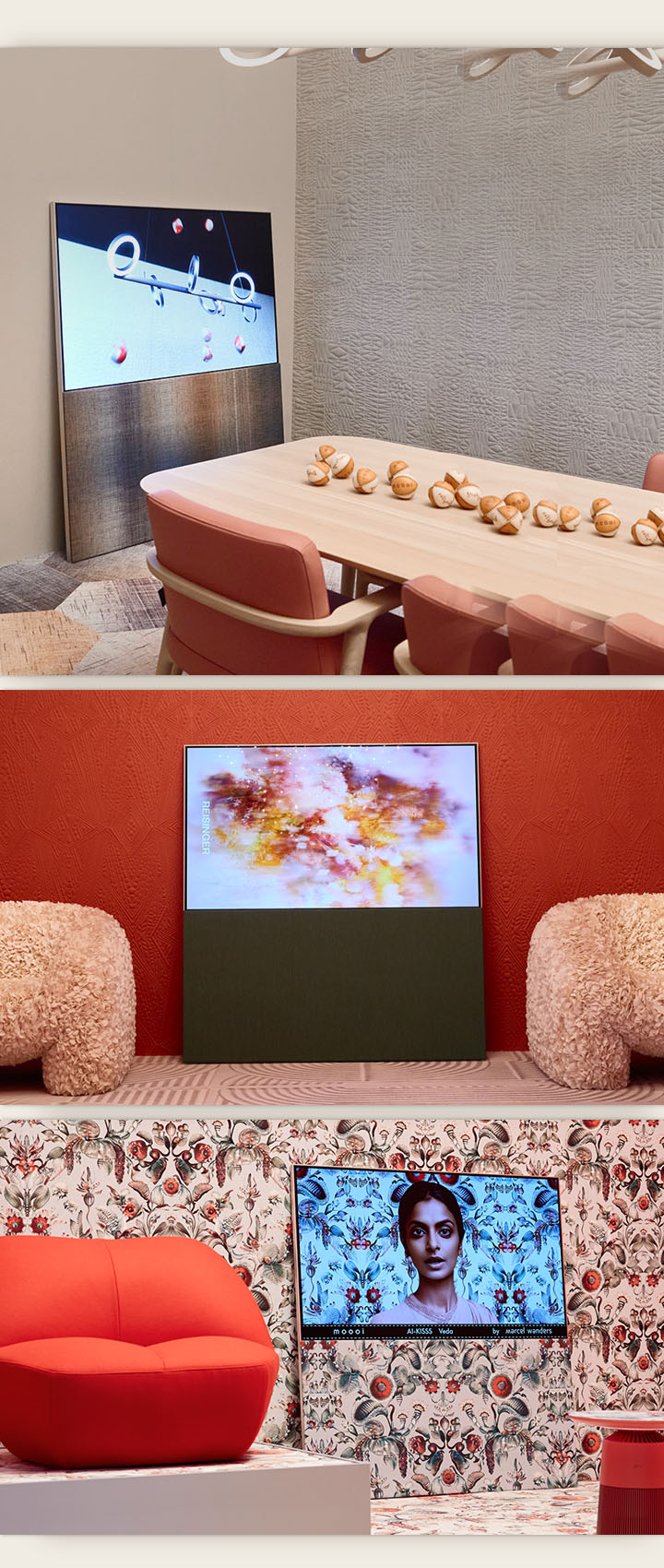 The top image shows Easel leaning against a wall in a neutral-colored room showing an abstract artwork featuring baseballs on the screen. Across from the TV sits a wooden table that also has baseballs on it. The bottom right image shows Easel leaning against a bright floral patterned wall with a red and green color scheme. A picture of a woman against the same background as the surrounding wall is on the screen. The fabric textured stand also has the same pattern. Beside the TV, there is a red one-person sofa. The bottom left image shows Easel leaning against a textured terracotta-colored wall. An abstract red, orange, and purple image fills the screen. On either side of the TV, there are beige, textured one-person sofas.