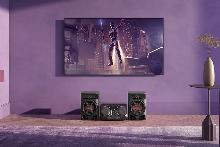 LG CK43N is placed on the living room. Above the speaker, a wall-mount LG TV is showing a movie scene.