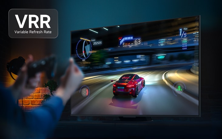 Bàn tay cầm bộ điều khiển trò chơi trước TV, trên màn hình là trò chơi đua xe. Logo VRR, tần số quét biến thiên được hiển thị.