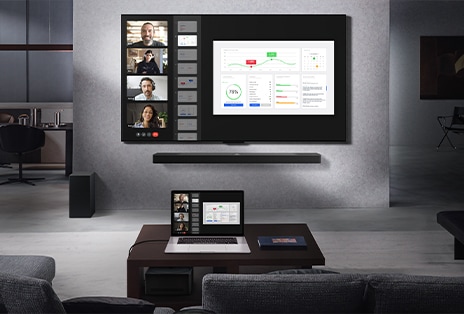 Phòng khách nhìn từ ghế dài, đối diện với TV LG True Wireless và LG Soundbar treo tường. Trên bàn cà phê là một chiếc máy tính xách tay được kết nối với Hộp kết nối không dây hầu như vô hình bên dưới bàn. Màn hình máy tính xách tay, hiển thị cuộc gọi video trực tiếp, được phản chiếu không dây trên màn hình TV. Toàn bộ không gian gọn gàng và không có sự lộn xộn của dây.
