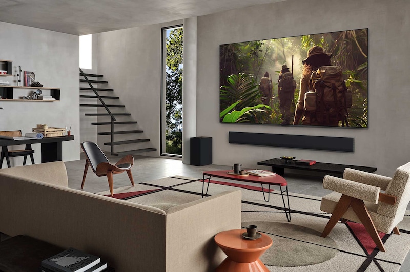 Wide view of a living room inside a premium home, a man is watching a movie on his wall-mounted LG OLED TV. The TV's design blends elegantly with the wall and the interior design.