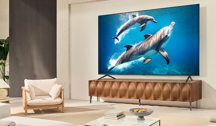 Một cô bé cùng chú chó đang ngồi trước chiếc TV LG QNED treo tường, trên màn hình là hình ảnh ba chú voi tiến lên, phía dưới là loa thanh LG.