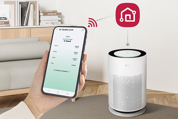 Trên hình ảnh là một bàn tay đang cầm điện thoại di động, bên trái hiển thị màn hình ứng dụng LG ThinQ, bên phải là logo LG ThinQ, và bên dưới là một máy lọc không khí Puricare được kết nối với điện thoại.