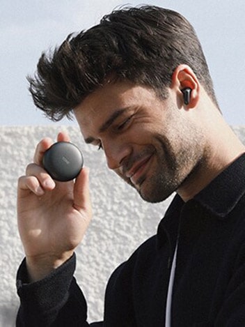 Side view of a smiling man wearing LG TONE Free Black and holding a cradle in his hand