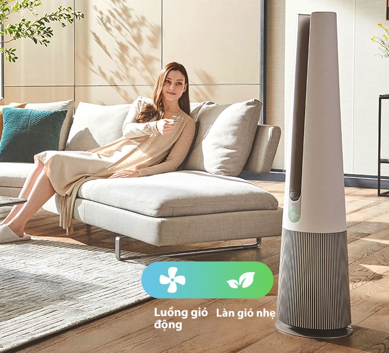 Một người phụ nữ ngồi trên ghế sofa trong phòng khách và đang dùng điều khiển từ xa của sản phẩm để thay đổi chế độ sản phẩm.