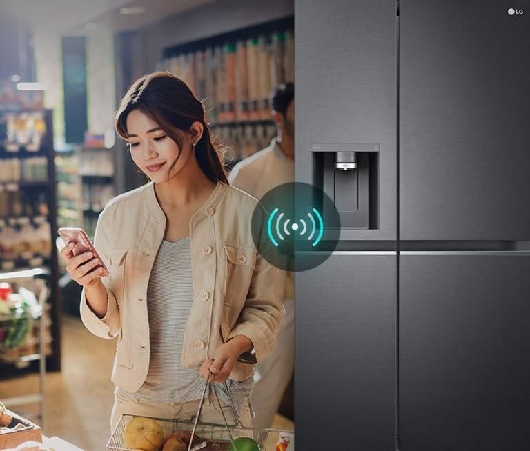 Một phụ nữ đang đứng ở cửa hàng và nhìn vào điện thoại. Mặt trước của tủ lạnh. Biểu tượng kết nối điện thoại và tủ lạnh