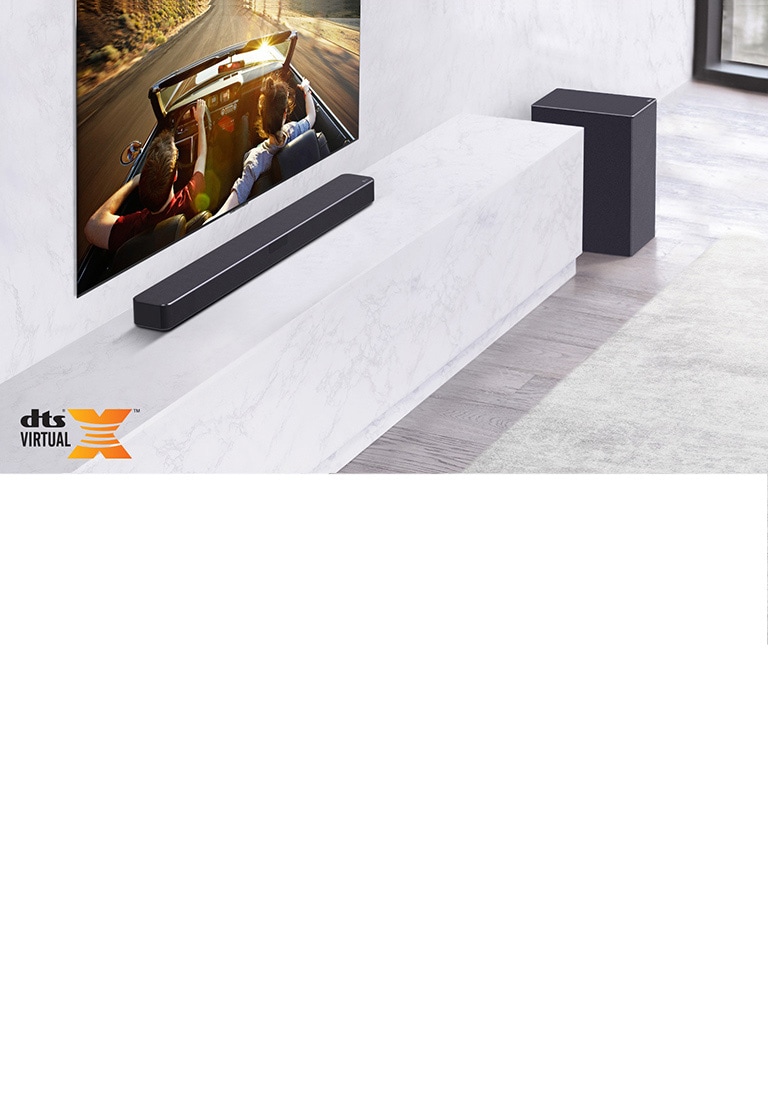 TV treo ở trên tường, loa thanh LG phía dưới, đặt trên kệ đá cẩm thạch trắng, có loa trầm ở bên phải. TV hiển thị một đôi nam nữ trong xe hơi.