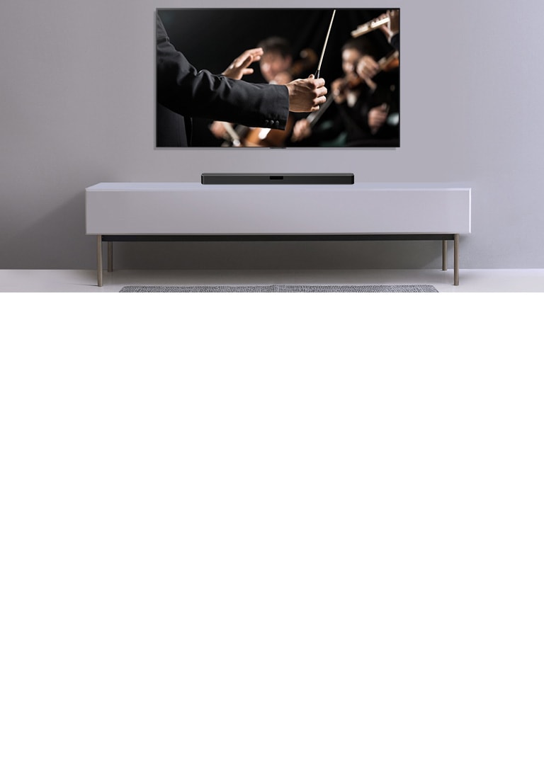 TV được hiển thị trên một bức tường màu xám và Loa thanh LG đặt bên dưới trên kệ màu xám. TV hiển thị một nhạc trưởng đang điều khiển dàn nhạc.
