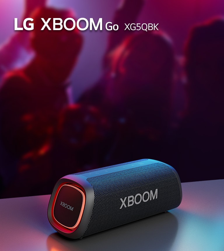 LG XBOOM Go XG5 đặt trên bàn kim loại với đèn màu cam. Sau chiếc bàn, mọi người đang tận hưởng âm nhạc.
