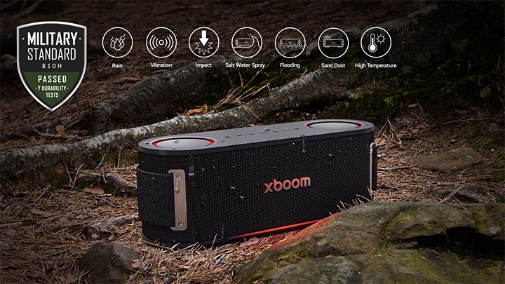 xboom Bounce được đặt trên mặt đất phủ lá ướt, giữa rễ cây và một viên đá. Ở góc trên bên trái là biểu tượng tiêu chuẩn quân đội.