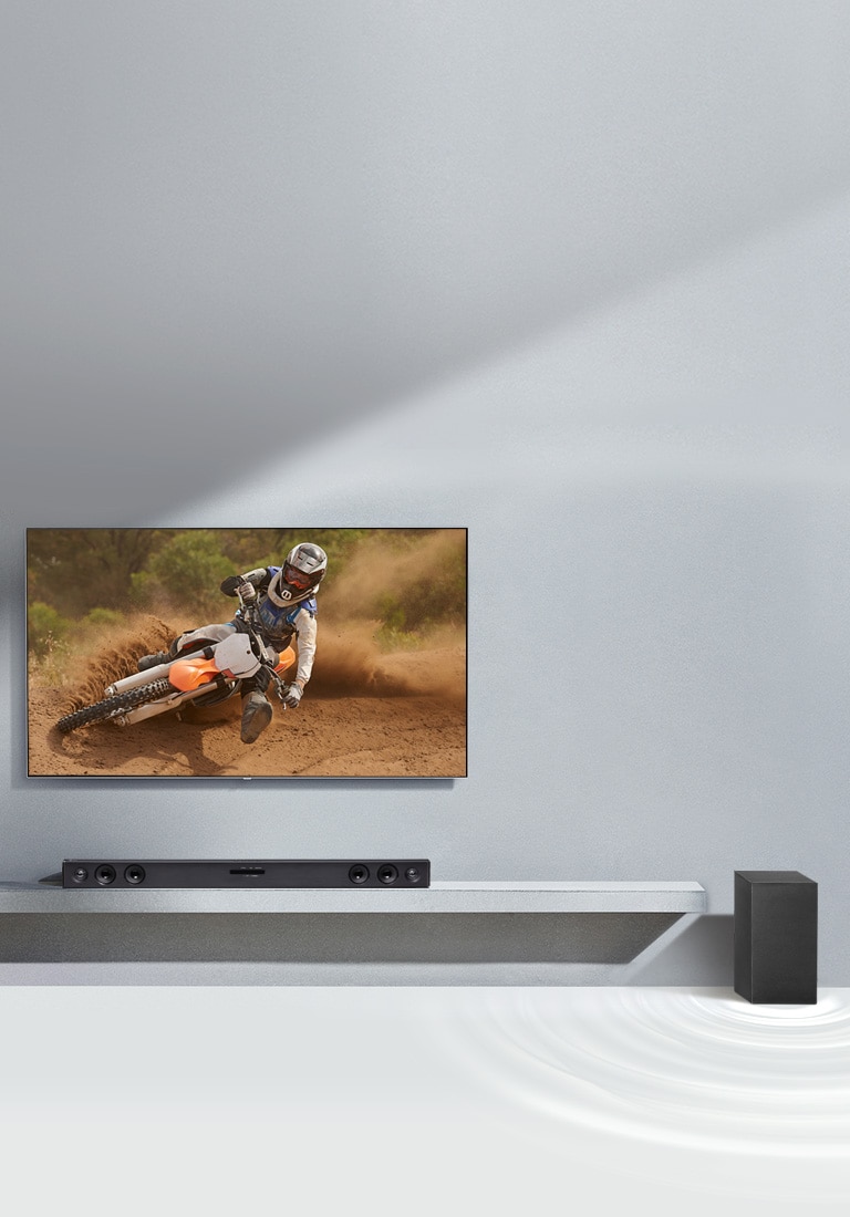 LG sound bar SQC2 and LG TV are placed together in the living room. The subwoofer is placed next to the sound bar. The TV is on, displaying a mortorcycle image.
