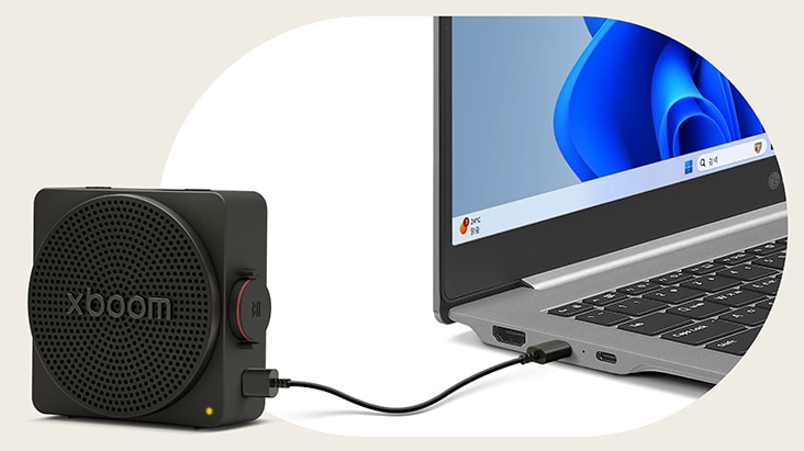 An LG gram laptop connected to the LG xboom Rock speaker via a USB-C cable, illustrating lossless audio playback through a wired connection.