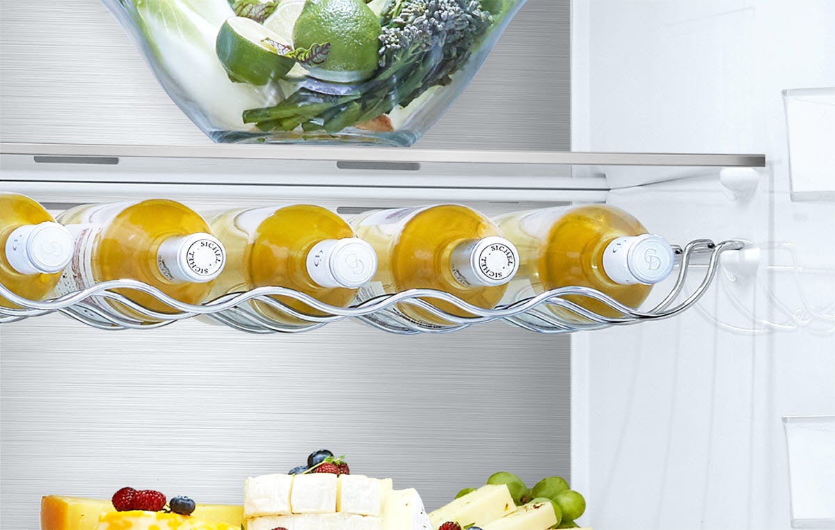 Five beverage bottles are placed in the wine rack that hangs under a shelf inside the fridge with other produce on the shelves surrounding.