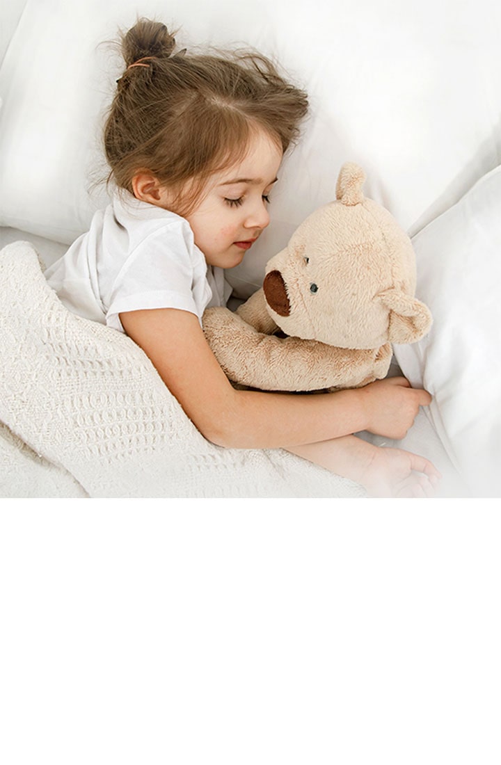 A little girl is lying in bed with a doll in her arms