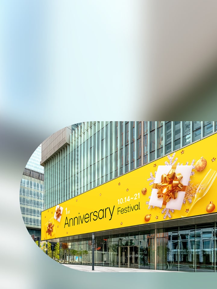 A bright yellow banner on a modern building promotes a 1st Anniversary Festival from October 14 to 21 with festive gift imagery.
