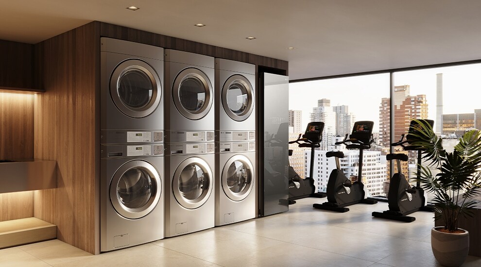 On-premises laundry room next to a fitness area with stacked washers and dryers overlooking the city