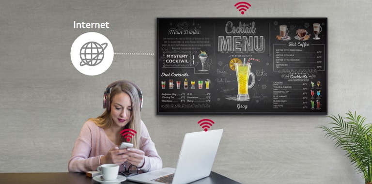 UL3J series is on the wall and a woman is using a personal PC and mobile phone. This image shows that the signage can operate as a virtual router so that the PC and mobile can be connected on the display to get wireless access.