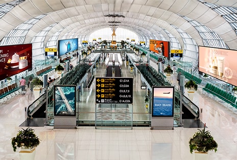 Esta imagem captura vários conteúdos reproduzidos em vários monitores dentro de um aeroporto.	