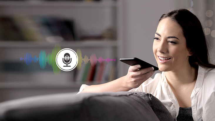 Uma mulher está controlando a TV falando ao controle remoto que tem reconhecimento de voz.