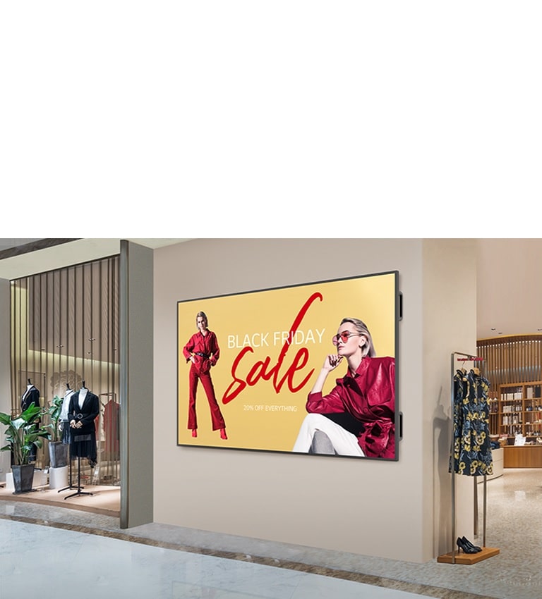 Um grande painel está instalado na parede interna de um shopping center, e a tela exibe anúncios com imagens claras e vibrantes.