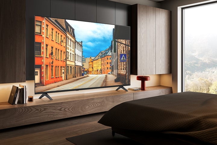 Uma TV está instalada em um quarto de hotel, exibindo uma cena de rua vívida.